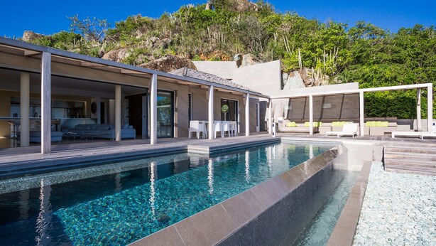 A modern pool area with clear water, surrounded by a covered patio with seating and a view of a natural landscape. - The One (2/3 Rooms) Luxury villa (Colombier)