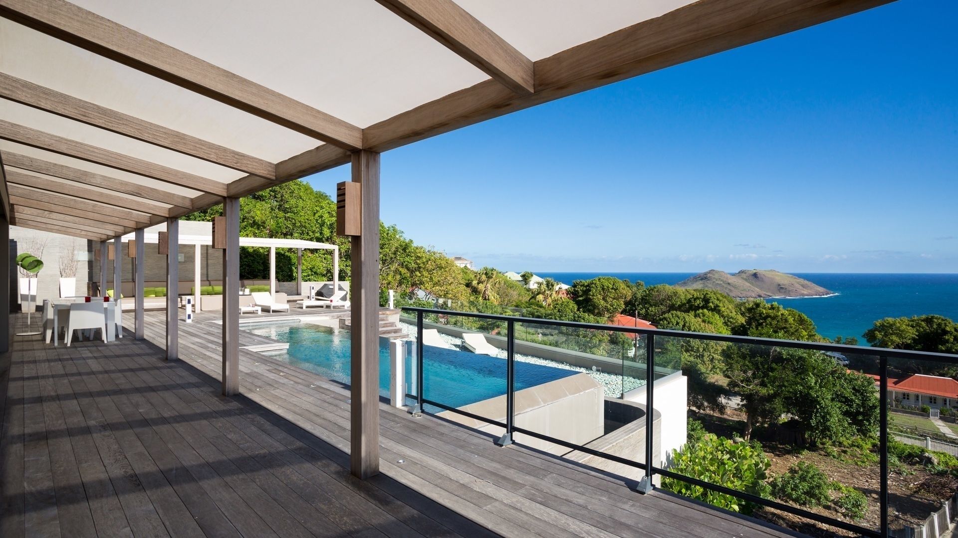 Eine Holzterrasse mit Pool, Sitzgelegenheiten im Freien und Blick auf den Ozean.