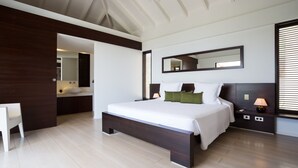 A modern bedroom with a large bed, a bedside table with a lamp, a mirror above the bed, and a view of the bathroom. - Beautiful The One Luxury villa (Colombier)