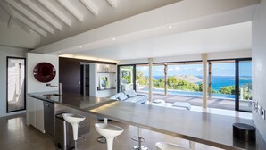 A modern kitchen with a central island, bar stools, and a view of the ocean. - Beautiful The One Luxury villa (Colombier)