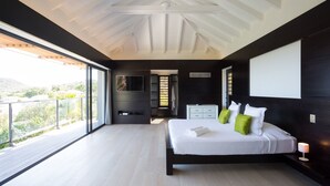 A modern bedroom with a large bed, a TV, and a balcony with a view of greenery. - Beautiful The One Luxury villa (Colombier)