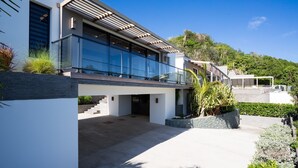A modern house with a glass facade, a covered outdoor area, and a stone retaining wall. - Beautiful The One Luxury villa (Colombier)