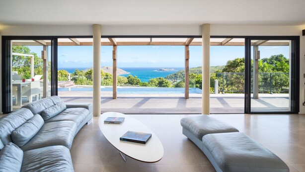 A spacious living room with a large window offering a view of the ocean and hills. - Beautiful The One Luxury villa (Colombier)