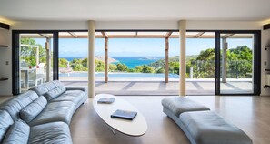A spacious living room with a large window offering a view of the ocean and hills. - Beautiful The One Luxury villa (Colombier)