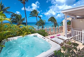 Un jacuzzi avec vue sur l’océan, entouré de palmiers et doté d’une terrasse en bois avec des chaises longues.