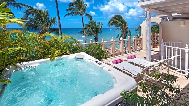 Un jacuzzi avec vue sur l’océan, entouré de palmiers et doté d’une terrasse en bois avec des chaises longues.