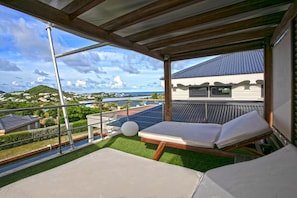 Un balcon avec deux fauteuils de jardin, une vue sur la côte et des panneaux solaires sur le toit.