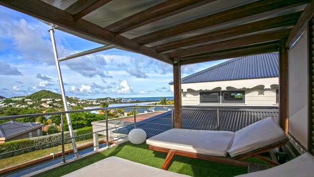 Un balcon avec deux fauteuils de jardin, une vue sur la côte et des panneaux solaires sur le toit.