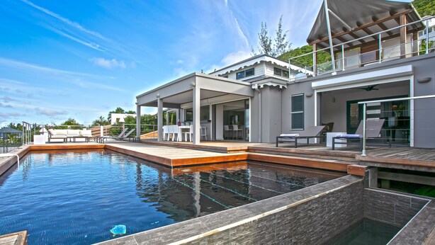 A modern house with a swimming pool, outdoor seating, and a covered patio.