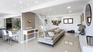 A modern living room with a sofa, dining table, and kitchen area.