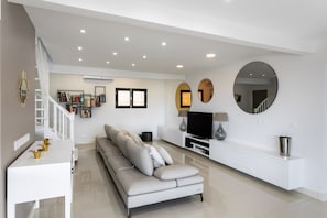 Een moderne woonkamer met een bank, een televisie en een witte console tafel.