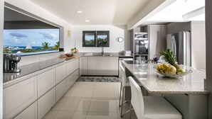 A modern kitchen with a view of the ocean, a window with a view, and a fruit bowl on the counter.