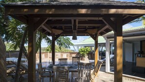 Uma pérgola de madeira com mesa e cadeiras sob ela, com vista para uma piscina e um edifício com telhado verde.