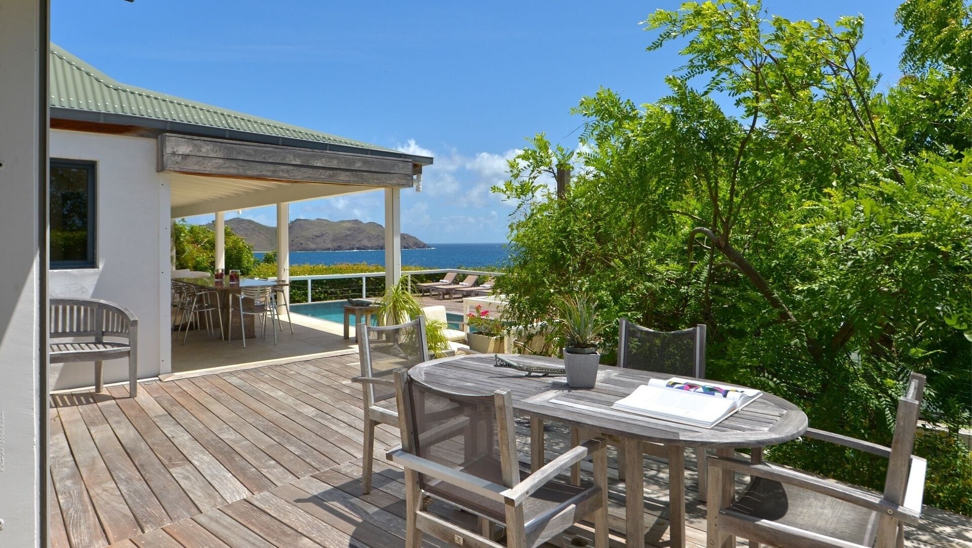 A wooden deck with outdoor seating, overlooking a pool and the ocean.