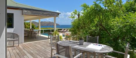 A wooden deck with outdoor seating, overlooking a pool and the ocean.