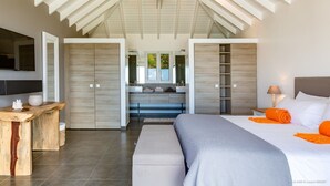 Een moderne slaapkamer met een groot bed, een houten bureau, een kaptafel met spiegel en een inloopkast.