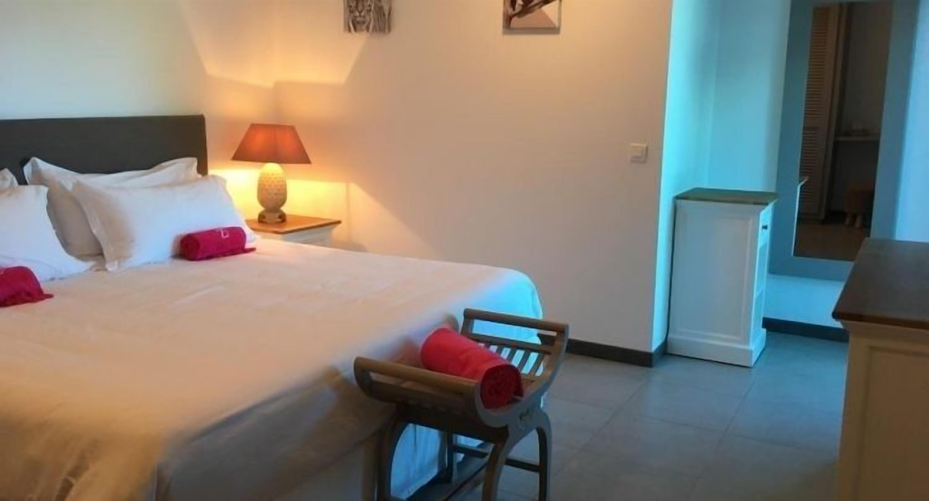 Une chambre d’hôtel comprenant un lit, une table de chevet avec une lampe, une chaise en bois et un petit meuble.
