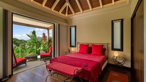 Ein Schlafzimmer mit einem großen Bett, roter Bettwäsche, einem Balkon mit Korbstühlen und Blick auf üppiges Grün.
