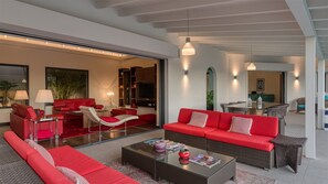 Uma sala de estar moderna com sofás vermelhos, uma mesa de centro de vidro e um espaço de jantar com mobiliário de vime.