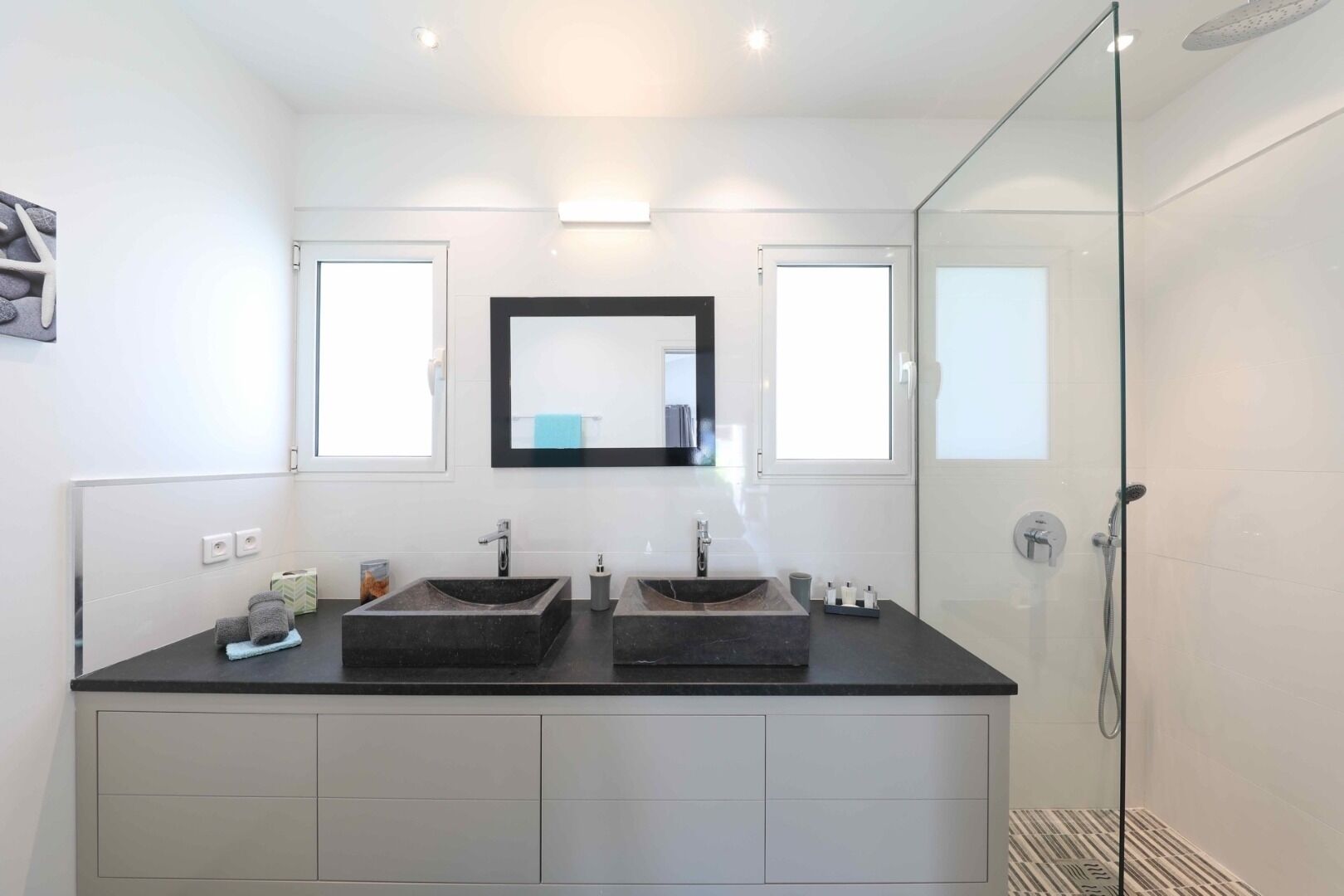 Ein modernes Badezimmer mit zwei Waschbecken, einem großen Spiegel und einer Duschkabine aus Glas.