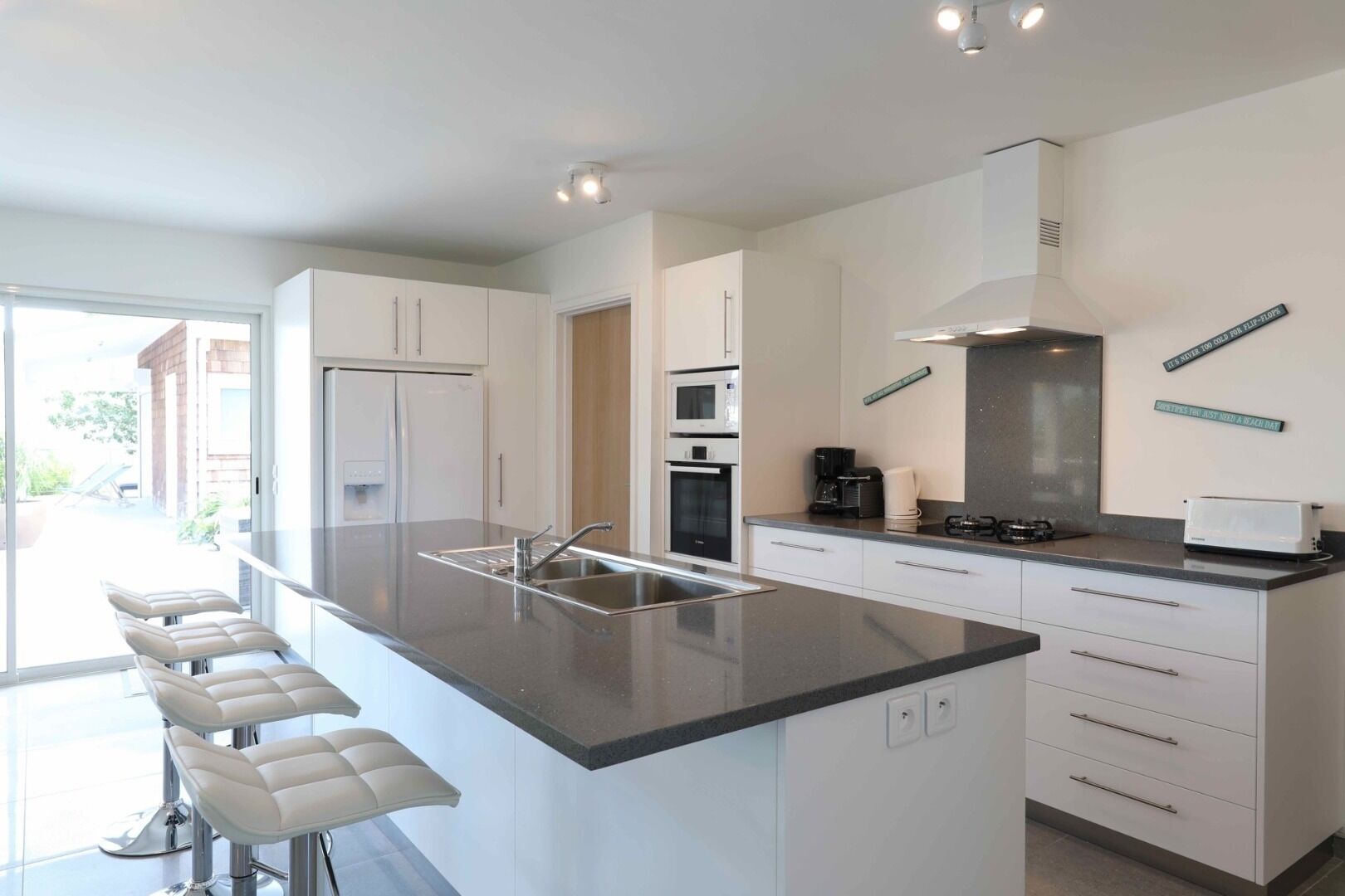 A modern kitchen with a central island, white cabinetry, and a large window providing natural light.