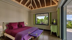 Un dormitorio con cama, televisor y ventana con vistas a la vegetación.