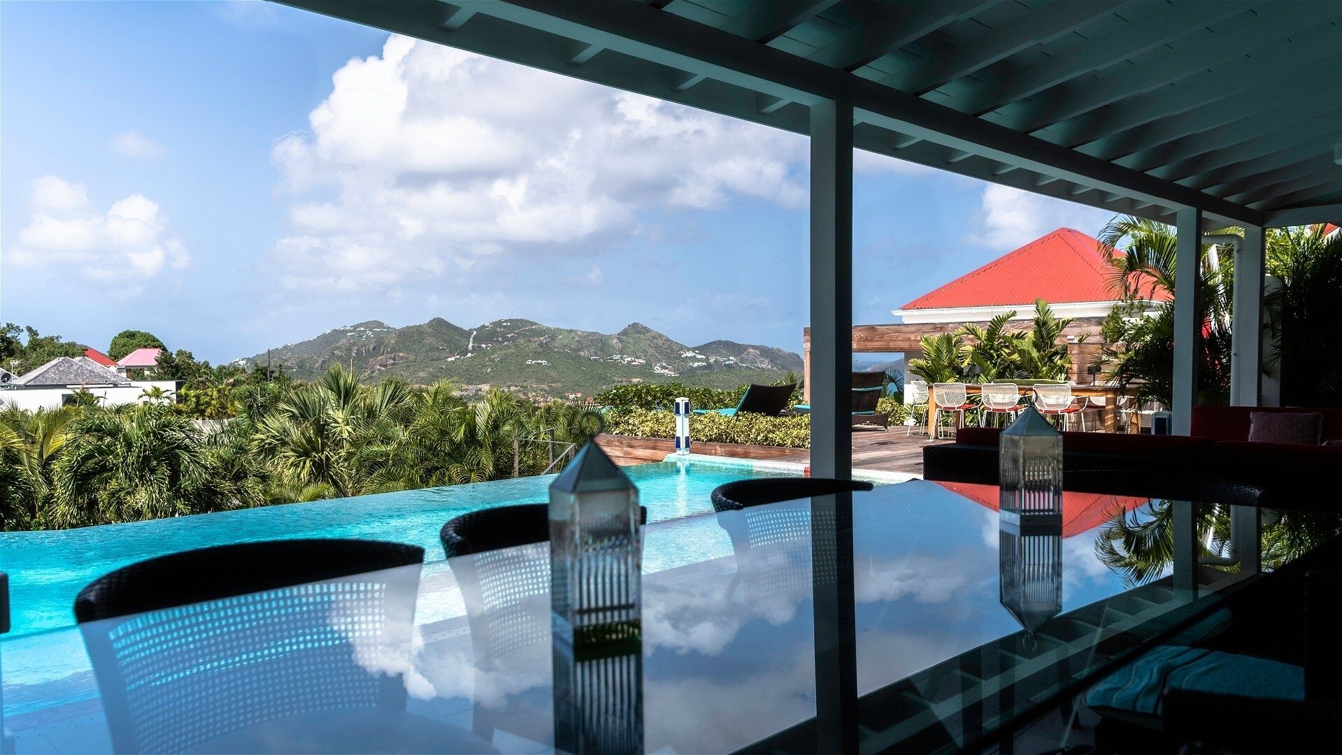 A pool area with clear blue water, lounge chairs, and a view of mountains and greenery.