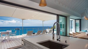 A modern outdoor deck with a kitchen area, seating, and a view of the ocean. - Passage (1/2 Rooms) Luxury villa (Gustavia)
