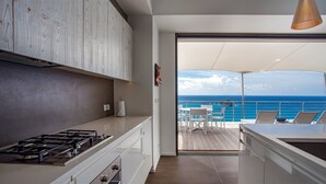 A modern kitchen with a gas stove, white cabinets, and a view of the ocean through a sliding glass door. - Passage (1/2 Rooms) Luxury villa (Gustavia)