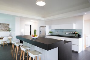 Une cuisine moderne dotée d’un îlot central, de tabourets de bar et d’un coin repas avec une chaise blanche.