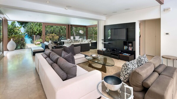 A modern living room with a large flat-screen TV, a glass coffee table, and a sofa set.