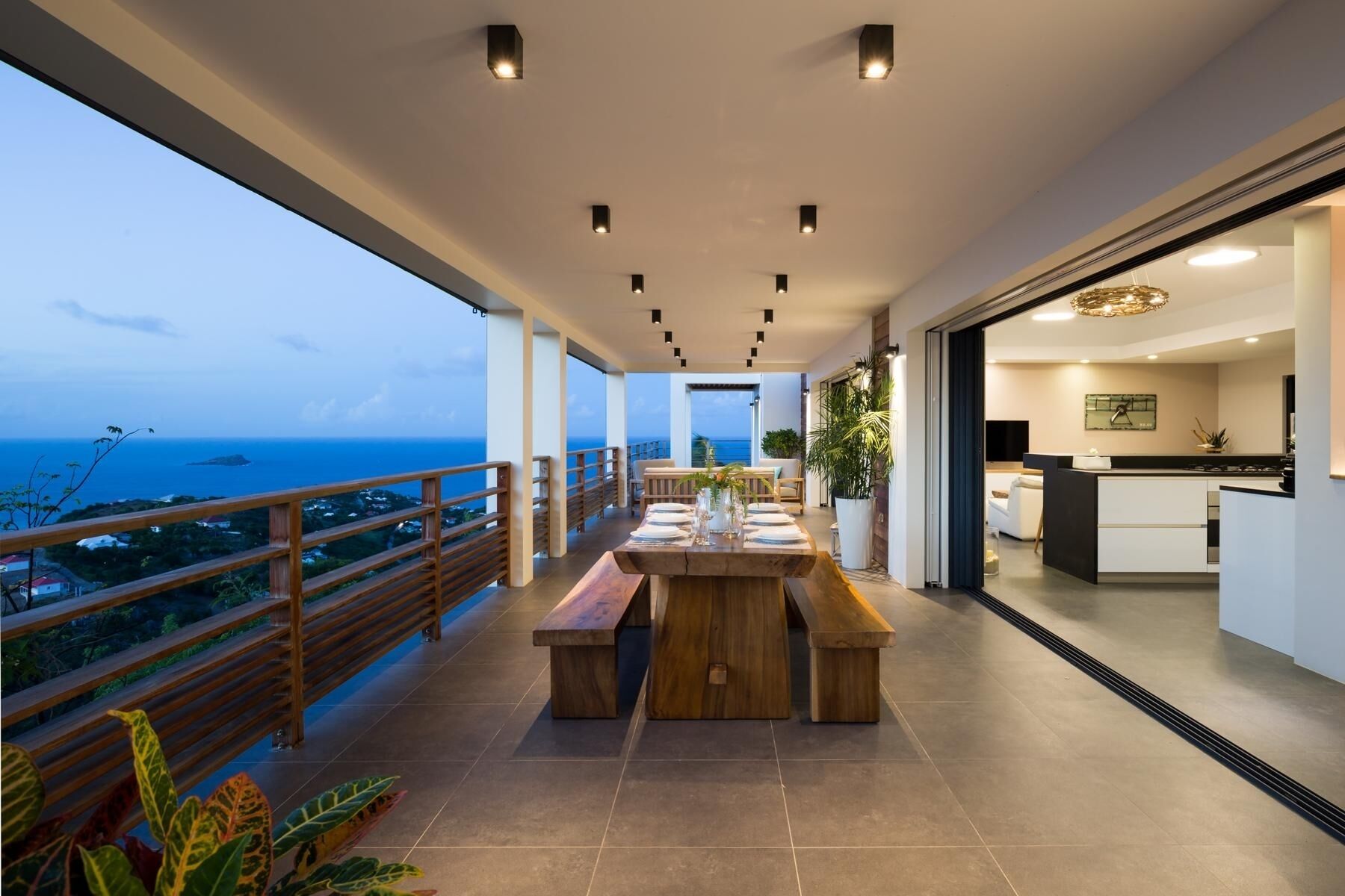 A modern outdoor dining area with a wooden table and benches, overlooking a scenic ocean view.