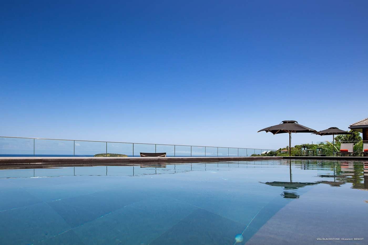 Una piscina cristalina con vista al océano, un área de descanso con sombrillas y un pequeño bote en la orilla.