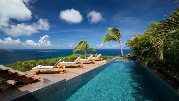 A pool with lounge chairs and palm trees, overlooking a clear blue ocean.