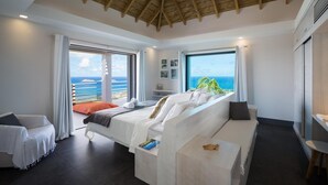 A modern bedroom with a large bed, a sofa, and a view of the ocean.