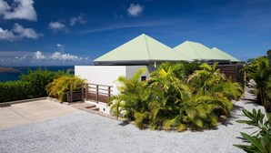 A modern building with a light green roof, surrounded by lush greenery and a clear view of the ocean.