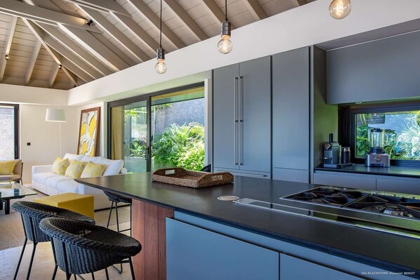 A modern kitchen with a central island, built-in appliances, and large windows offering views of greenery. - Blackstone (2/6 Rooms) (Marigot)