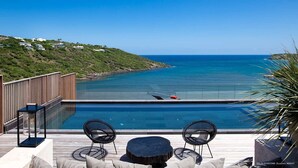 Un área junto a la piscina con vistas al océano, sillones de descanso y una terraza de madera.