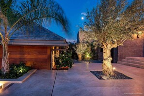 A modern house with a sloped roof, a wooden exterior, and a well-lit garden area at dusk.