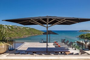 A deck with a large umbrella, lounge chairs, and a view of the ocean.