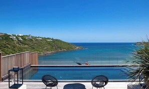 Una piscina con vista al mar, una terraza de madera y dos sillas.