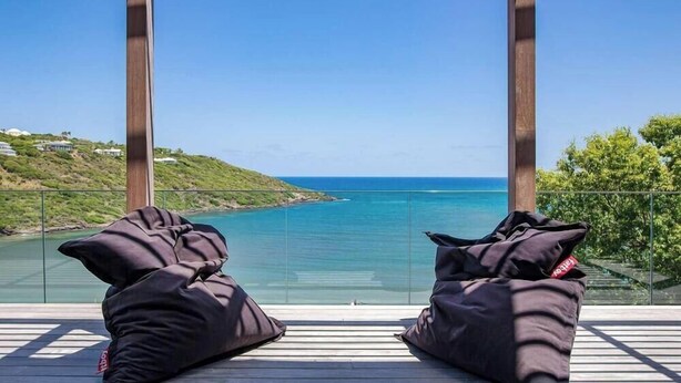 A balcony with two black bean bags, overlooking a coastal view with clear blue water and a hilly landscape. - Blackstone (4/6 Rooms) (Marigot)