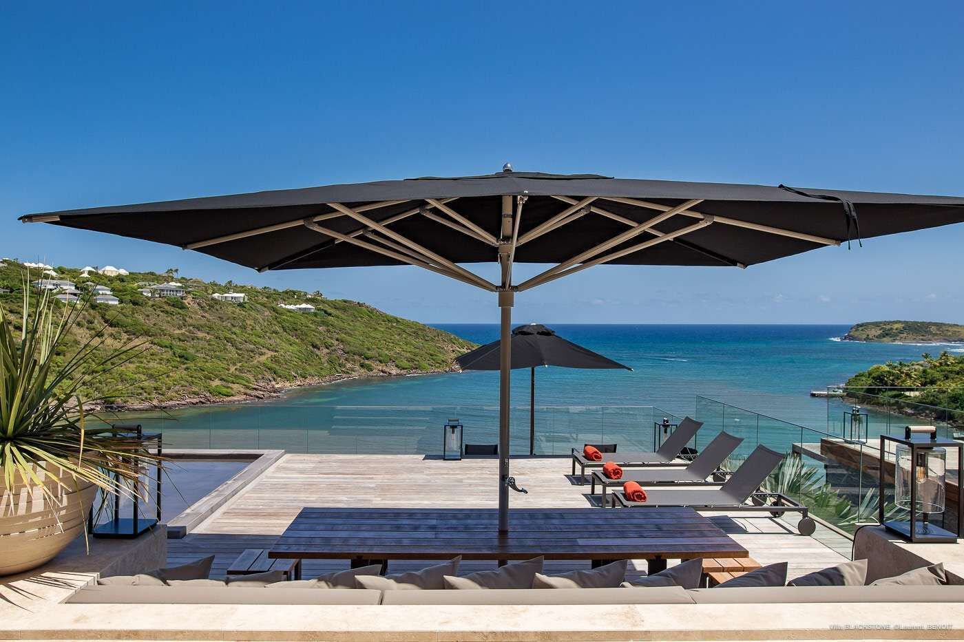 A deck with a large umbrella, lounge chairs, and a view of the ocean.