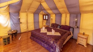 Quarto em estilo tenda com uma cama, mesas de cabeceira e uma mesinha com abajur.