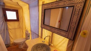 Casa de banho com lavatório estampado, espelho com moldura decorativa, sanita e janela.