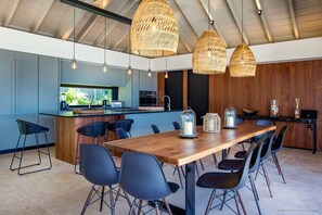 Een moderne keuken met een houten kookeiland, zwarte stoelen en hangende rieten hanglampen.