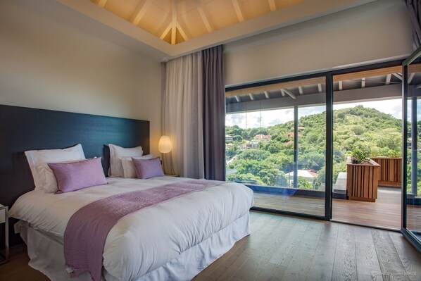 Une chambre moderne avec un grand lit, une vue sur un paysage verdoyant et une porte-fenêtre coulissante donnant sur un espace extérieur.