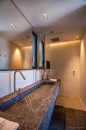 Une salle de bain moderne avec un long lavabo en marbre fonc é, un grand miroir et des spots encastrés au plafond.
