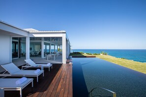 Una casa moderna con piscina, sedie a sdraio e vista sull'oceano.