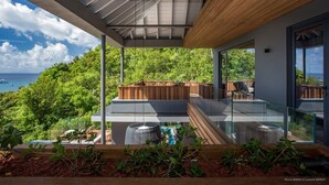 A modern outdoor balcony with a glass railing, wooden deck, and lush greenery. - Beautiful Sasha Luxury villa (Corossol)